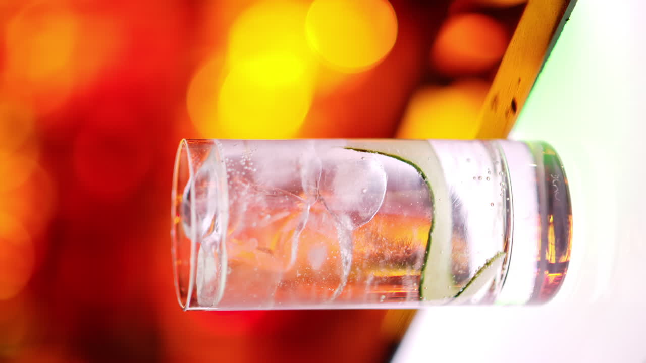 Close up cocktail with ice at the bar at night with red neon lights, slow motion vertical screen