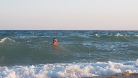 Aufgeregtes-Kind-Schwimmt-Bei-Sonnenuntergang-Im-Welligen-Meer