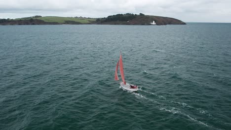 Small-classic-yacht-with-red-sails,-on-a-cloudy-gloomy-day