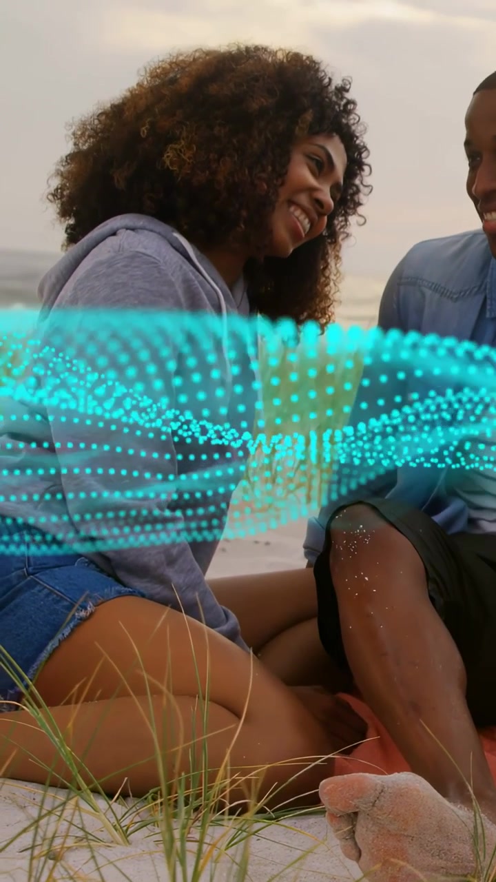 Couple sitting beach, teal wave sweeping, obscuring torsos and guiding leaning closer for marketing
