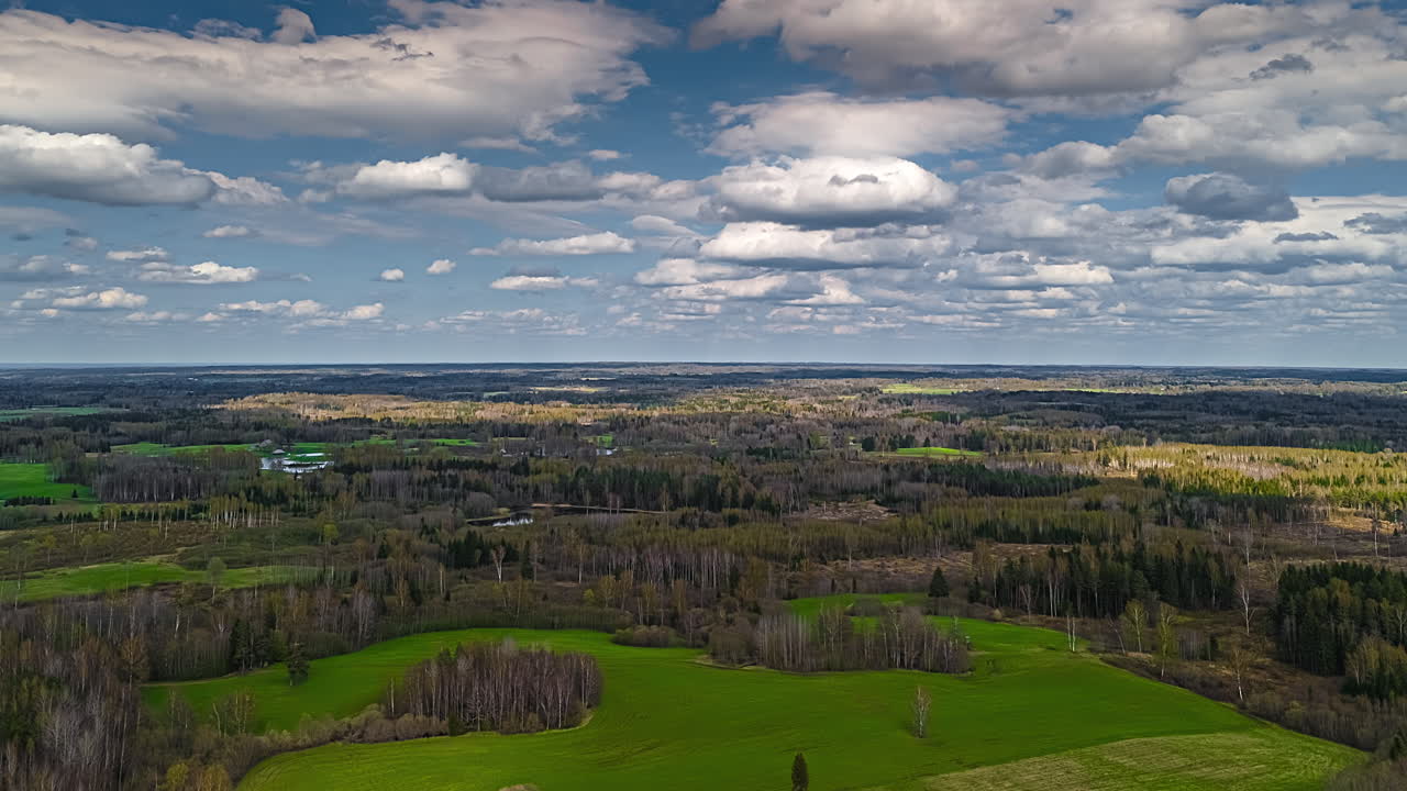 Farm crops growing in a forested landscape with a dreamy cloudscape above - aerial time lapse