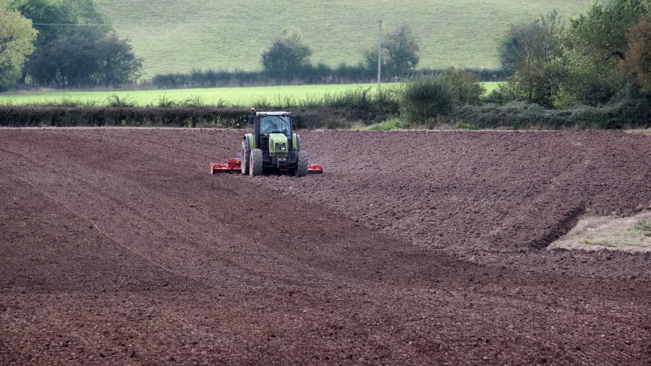 un agricultor conduciendo un tractor labrando y rastrillando un campo arado durante el otoño en la campiña de worcestershire, inglaterra
