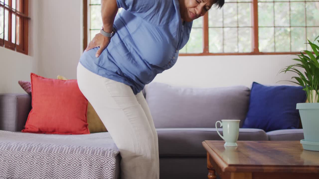 집 에서 소파 에서 일어나는 동안 아픈 등 을  ⁇ 고 있는 아시아 여성