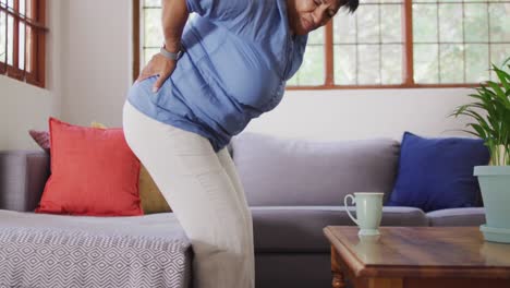 asian senior woman holding her back in pain while getting up from a sofa at home
