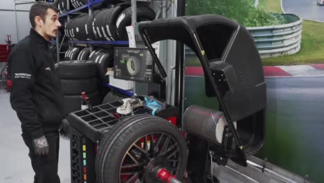 técnico de taller de neumáticos en uniforme usando una máquina de equilibrio de ruedas automáticas para reparar la rueda