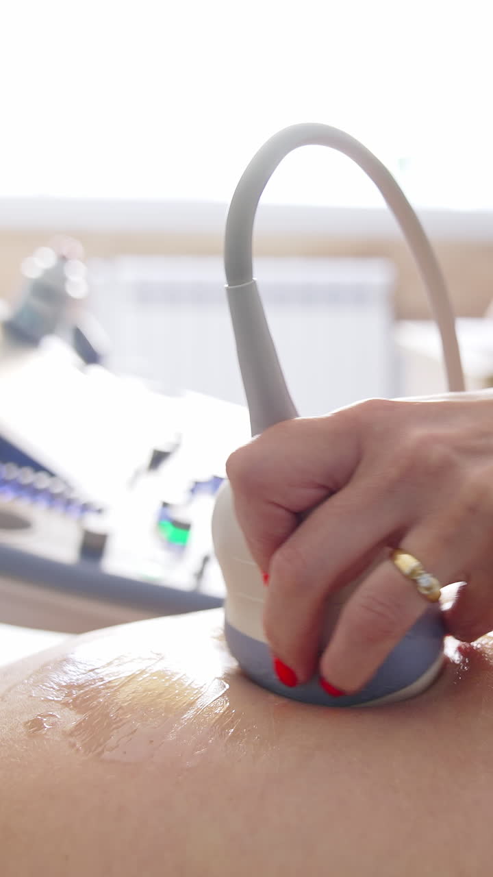 Female doctor examining belly of pregnant woman with ultrasound. Gynecologist moving transducer on abdomen of a future mother in clinic during ultrasonography process. Vertical video
