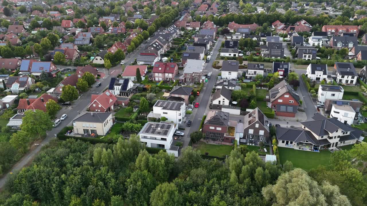 Moderne enfamiliehuse med solpaneler på taget i skumringen. Forstadskvarter i en tysk by om sommeren. Bredt luftfoto fra siden. Tema: Vedvarende energi.