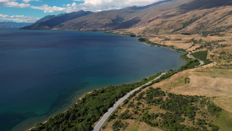 aerial drone pan shot over mountain range surrounding lake hayes in wakatipu in central central queenstown, new zealand at daytime