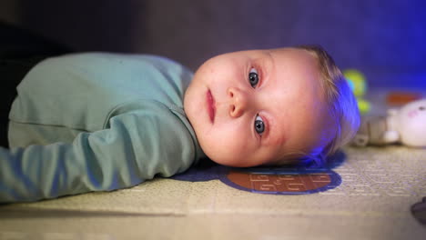 beautiful blond baby boy lying peacefully on the floor. infant child with big blue eyes close up portrait.