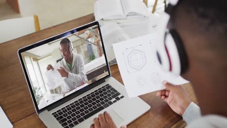 African-american-male-college-student-holding-notes-while-having-a-video-call-on-laptop-at-home