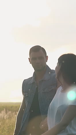 pretty girl in white t-shirt walks on yellow field holding man in denim vest hand at summer sunset slow motion