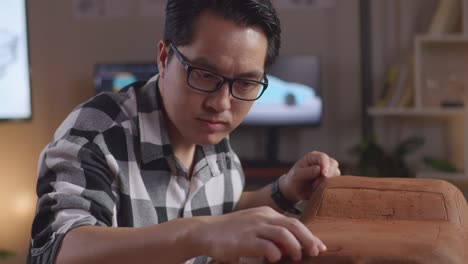 close up of asian man automotive designer works on the sculpture of car clay using his hands to smooth out the surface and create details in the design in the studio