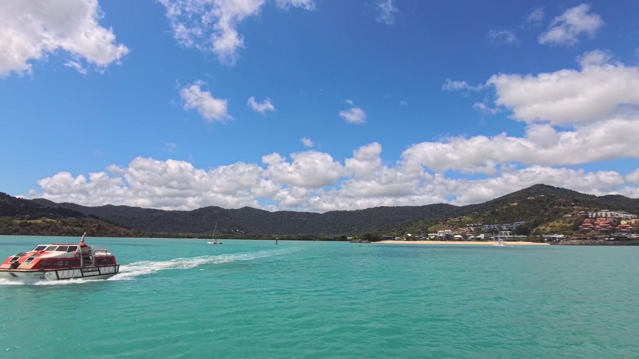 Barco navegando por aguas turquesas con montañas tropicales y un pueblo