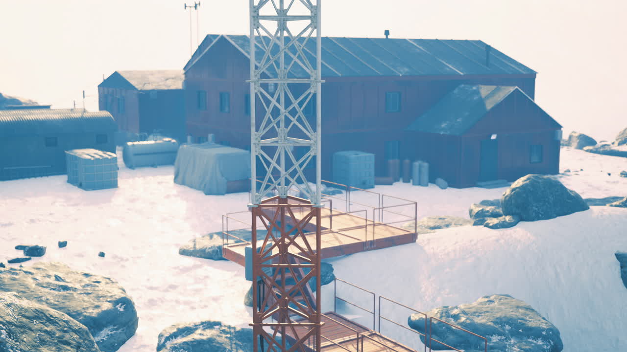 A communication tower stands near several red buildings in a snowy environment