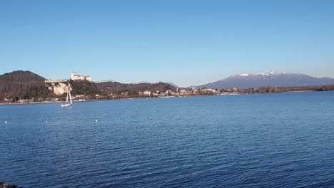 small sailboat sailing on maggiore lake in piedmont with mountains and castle in background. italy