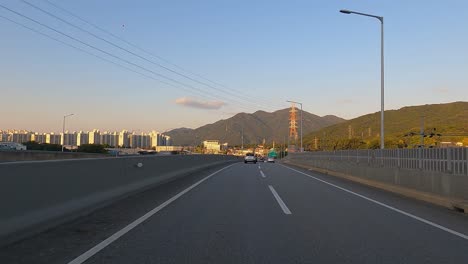 driving on the road with view of apartment blocks and mountains in autumn foliage. sunset in seoul, south korea. pov