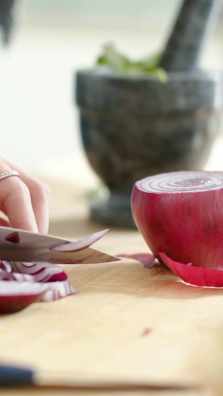 Vertical video: Slicing cook hand red onion with chef knife on board reaching for herbs for cooking