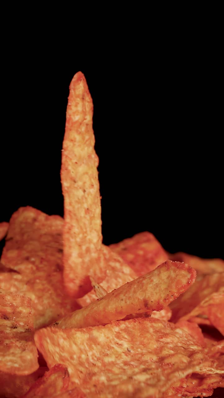 Ludzka dłoń podnosi trójkątny chips nacho ze stosu chrupiących przekąsek, zbliżenie, dramatyczne oświetlenie.