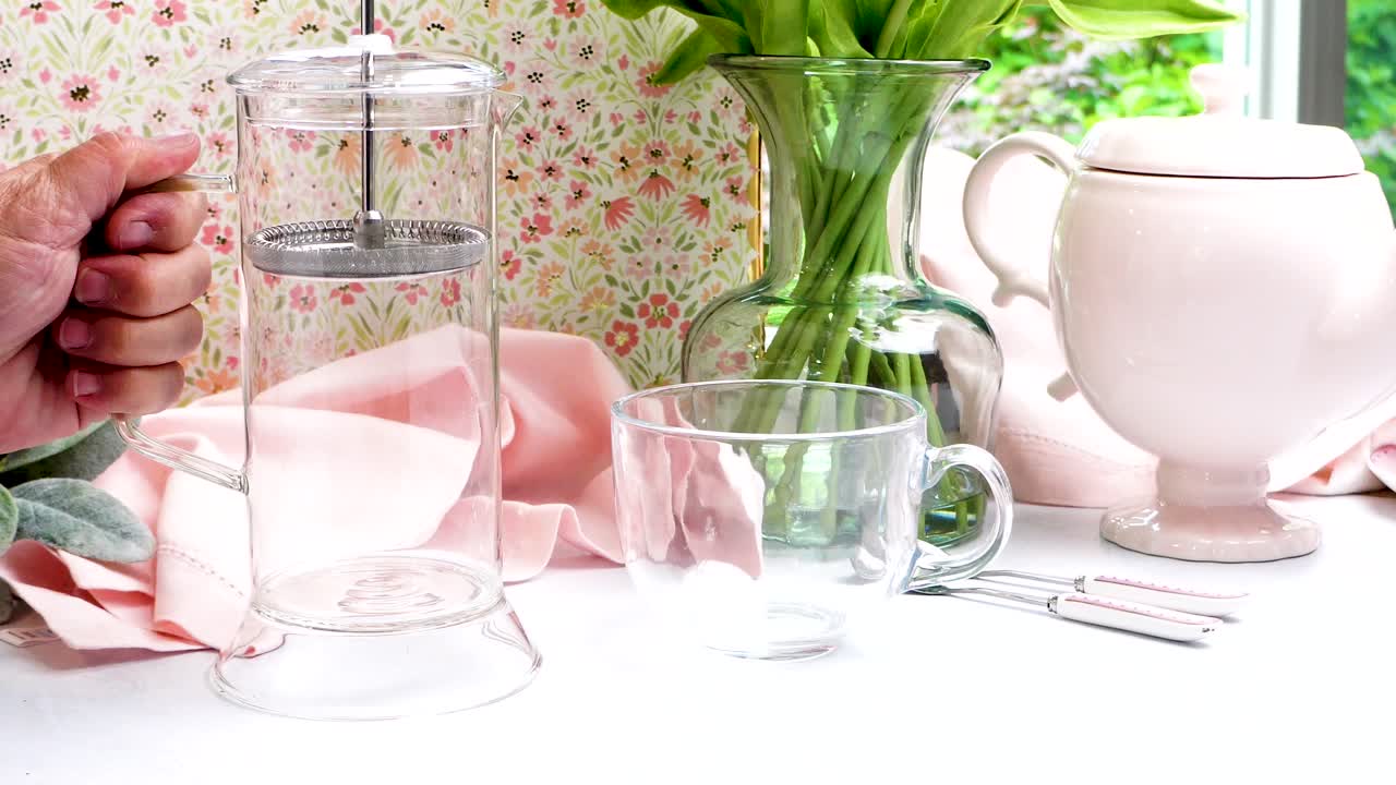 French Press made of clear glass being used to make a hot coffee. Pastel colors in a scene making hot coffee. Fresh ground coffee for brewing using a French Press method of extraction.