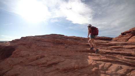 young woman with backpack walking on red sandstone hills on hot sunny day