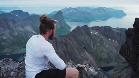 male hiker sitting on a mountain and looking out over a lake in kvaenan, norway - close up