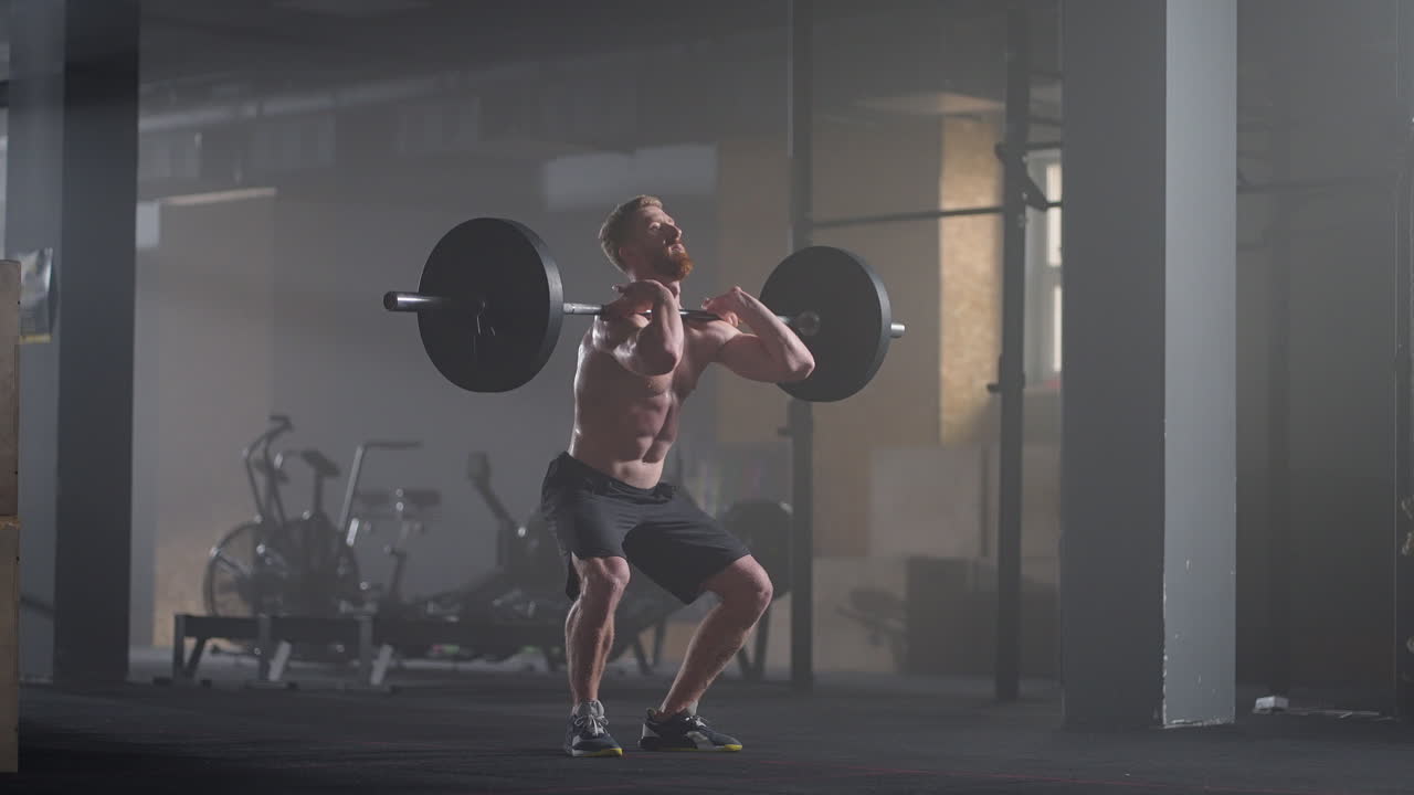 Rallentatore: uomo fitness culturista si allena con un bilanciere, esercizi di sollevamento pesi, sportivo muscoloso che pratica powerlifting con pesi pesanti, esegue squat in palestra godendosi uno stile di vita sano.