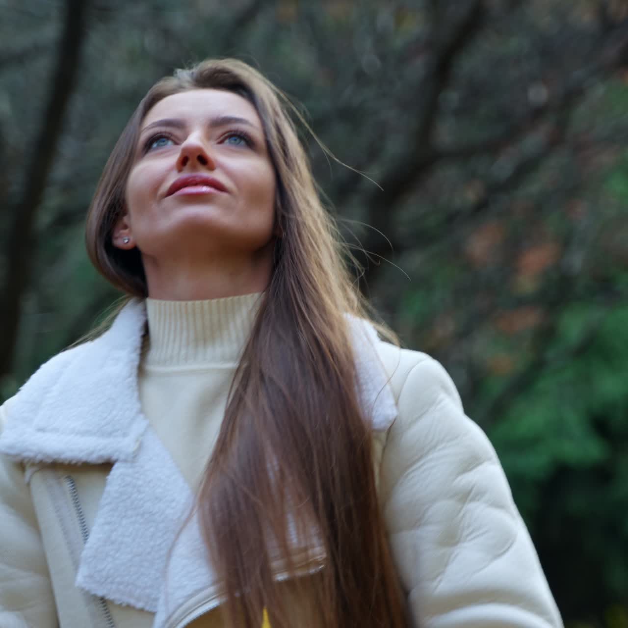 Attractive Caucasian lady holding a bouquet of colorful leaves. Smiling girl throws the bunch of leaves into air happily. Autumn park backdrop