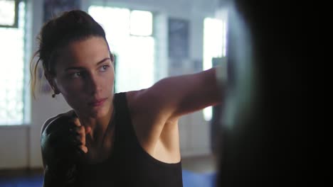 close up view of caucasian female boxer hitting the boxing bag with her hands in gloves in the gym with smoke. tough power