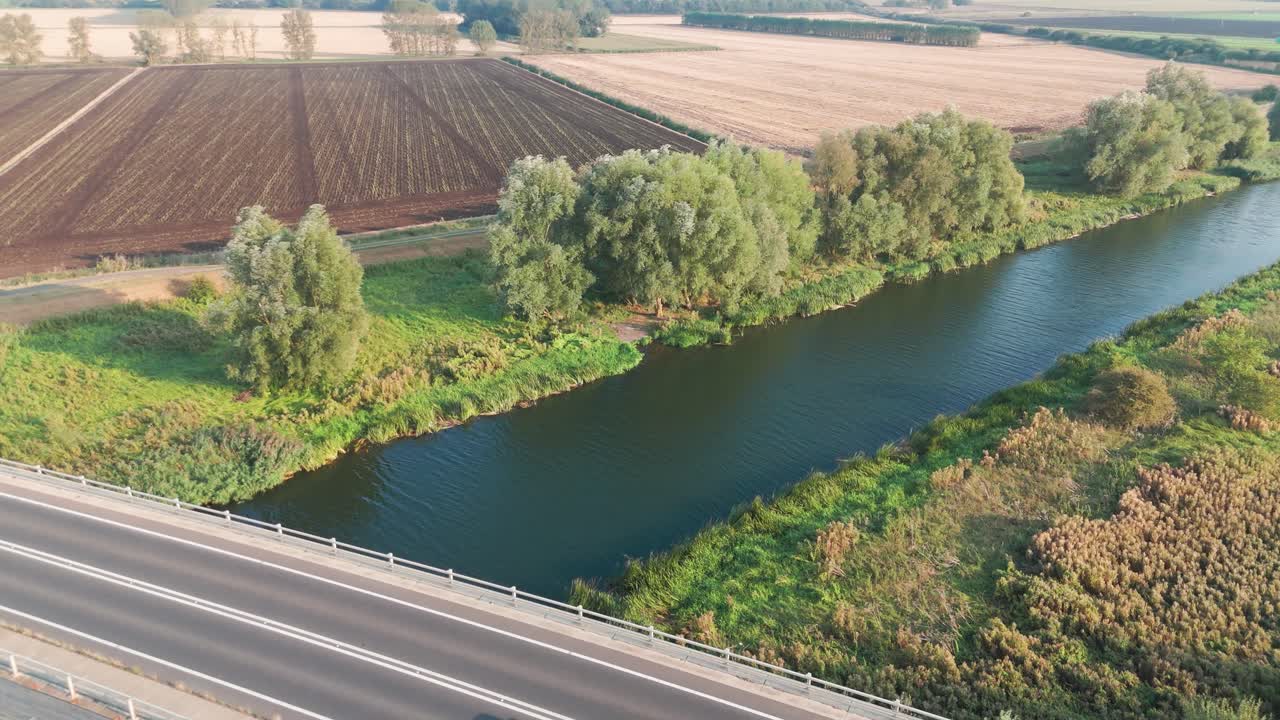 Aerial view of a bridge over a river with cars passing, surrounded by agricultural fields and natural scenery, showcasing a blend of infrastructure and rural landscape