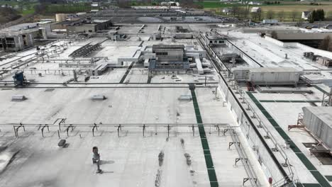 drone flyover rooftop of large industrial factory with pipes and steel construction in usa