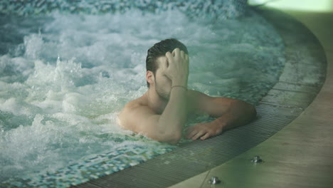 Chico-Sexy-Relajándose-En-La-Piscina-Del-Hotel-Spa.-Hombre-Tocando-El-Cabello-Mojado-En-El-Jacuzzi-Del-Spa.