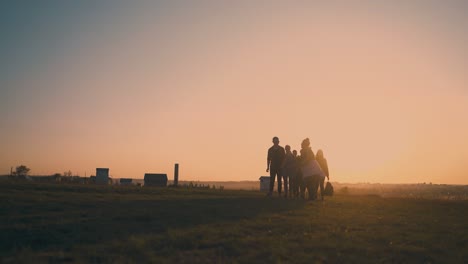 joyful-friends-walk-on-bank-to-modern-camp-at-back-sunset