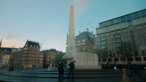 dam square in amsterdam highlights the national monument surrounded by historic buildings and early morning activity. pedestrians and cyclists pass by this iconic dutch plaza. amsterdam, nederland