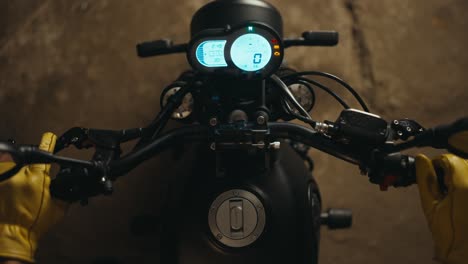 Close-up-top-view-of-a-mechanic-in-yellow-gloves-starting-a-motorcycle-and-inspecting-its-glowing-panel-in-the-workshop