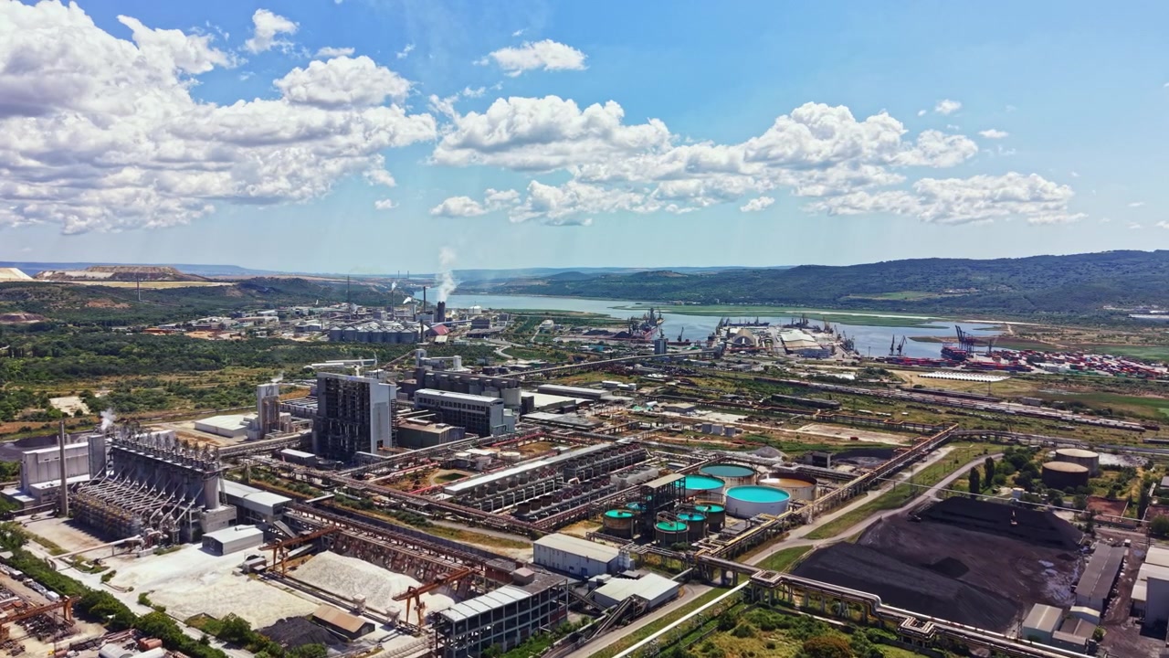 Vista de una gran zona industrial con fábricas, ríos y zonas verdes bajo un cielo azul con nubes al fondo.