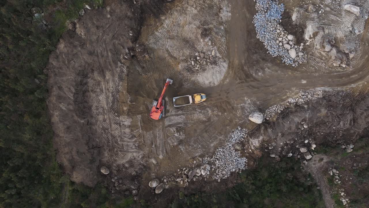 aerial - excavator loading soil into truck during land clearing operations at construction site