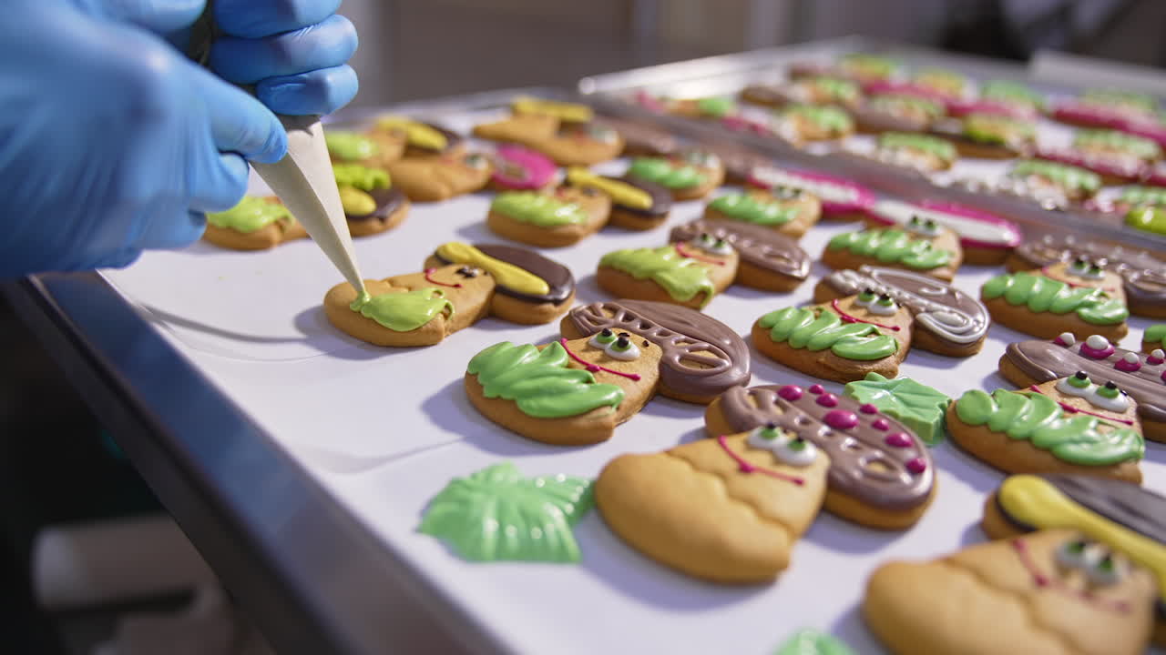 Beautiful tasty biscuits on the metal trays. Hands of confectioner squeeze decoration cream on the cookies. Close up.