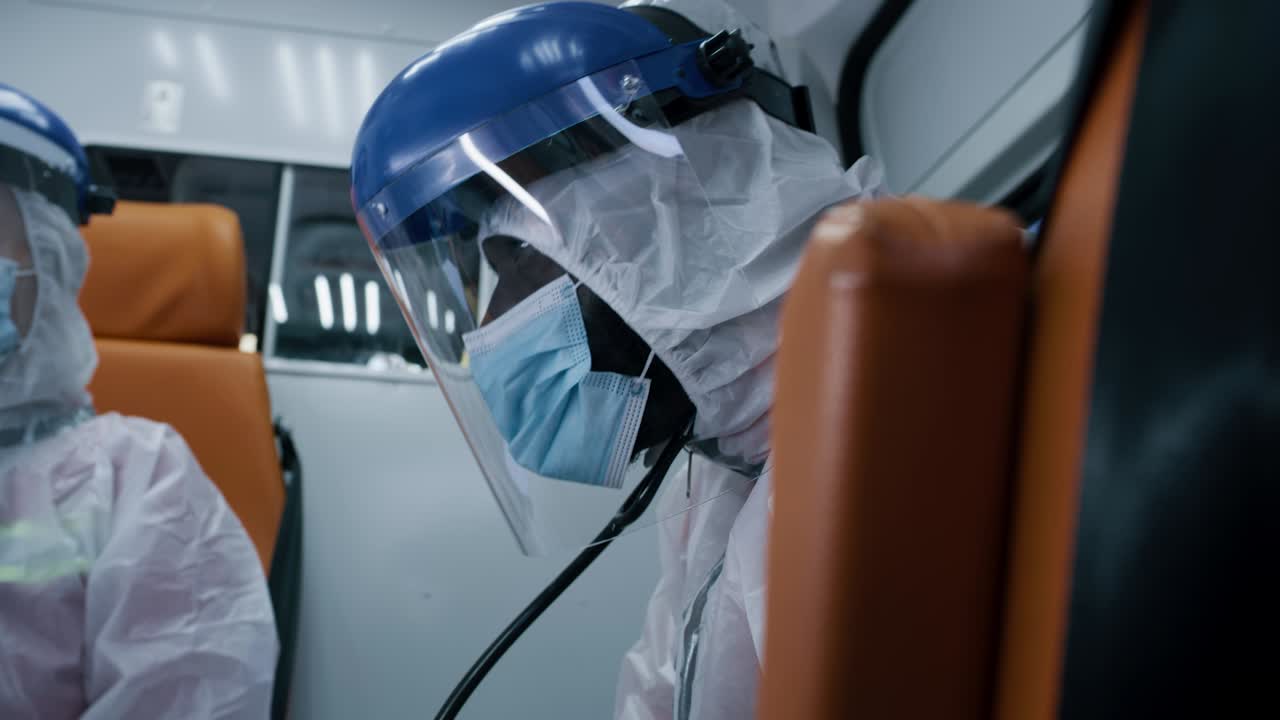 black Paramedic Riding Ambulance with Colleague Low Angle of Tired African American Male Doctor in Hazmat Suit Sitting Near Female Colleague while Riding Ambulance during Coronavirus Pandemic