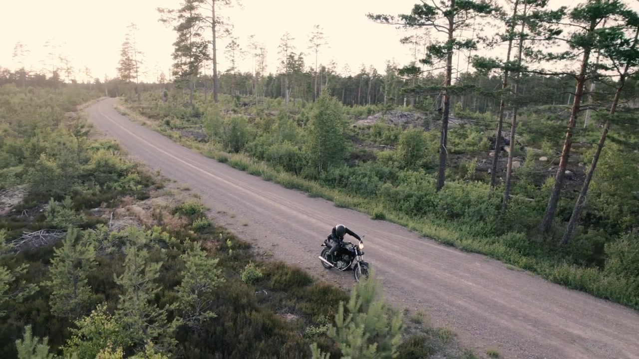Un ragazzo sale su una moto, l'accende e si allontana verso il tramonto, con un drone che sorvola.
