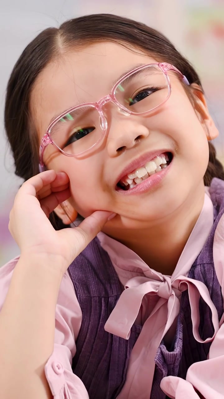 A happy young girl wearing pink glasses poses playfully with a cheerful classroom background