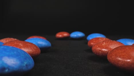 macro push in shot of button-shaped red and blue candy with a black background