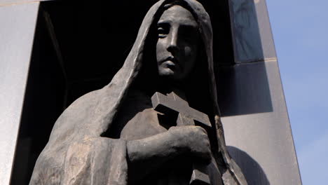 woman holding cross made of black stone statue in la recoleta cementery at daytime tight shot