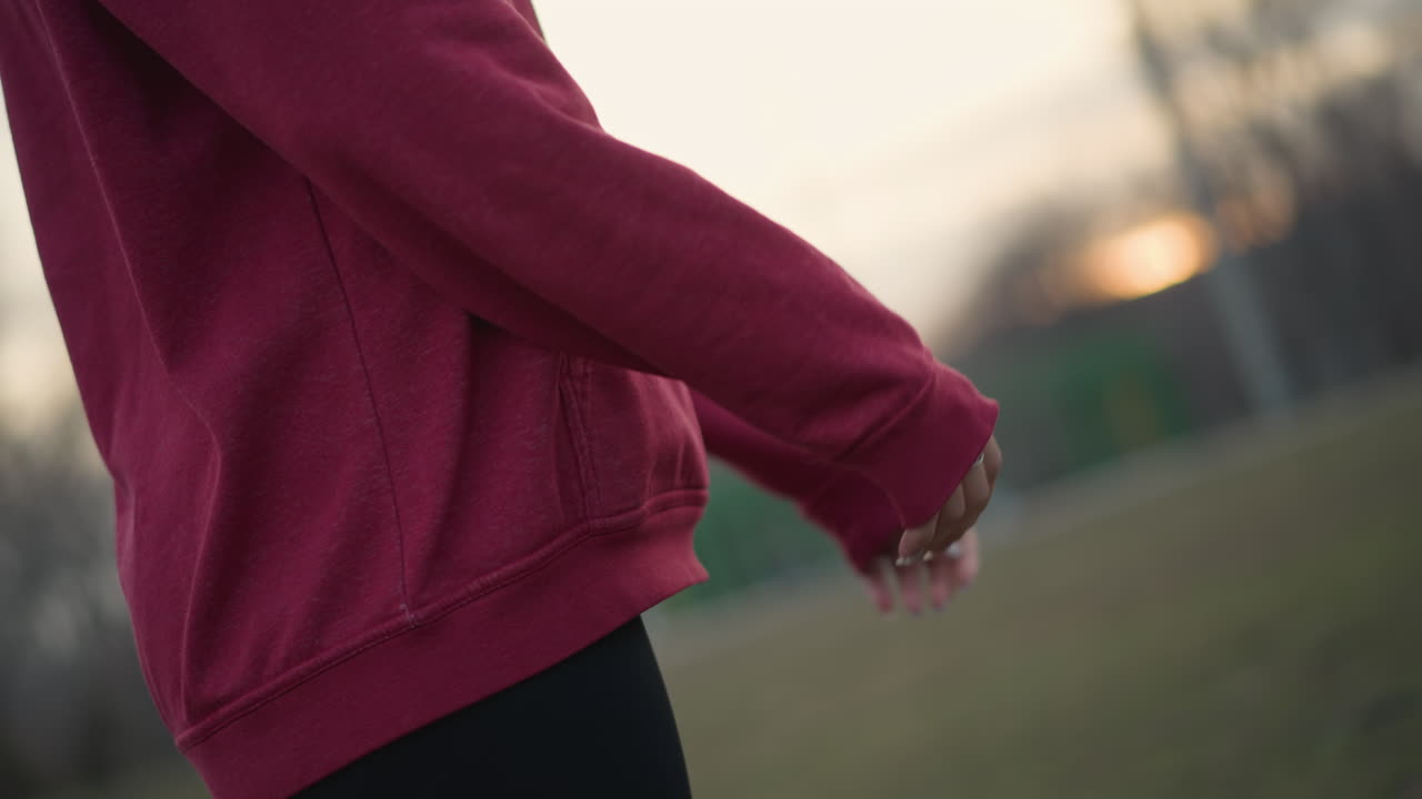 Arms Stretch Sunset, Evening Park Warmup With Hoodie, Relaxed Arms Extend During Dusk In Peaceful Park Setting, Gentle Stretching Of Arms At Sunset In Tranquil Park Before Running Begins