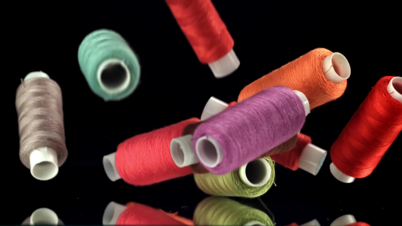 Colorful Spools of Thread Falling and Landing on a Reflective Black Surface