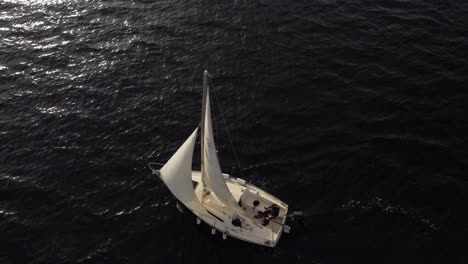 Aerial-of-a-white-sailboat-drifting-in-dark-dramatic-sea-water-creating-ripples