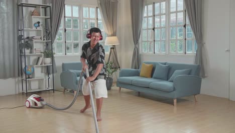 cheerful asian boy cleaning up his home and singing, he is using the vacuum cleaner as a guitar and microphone