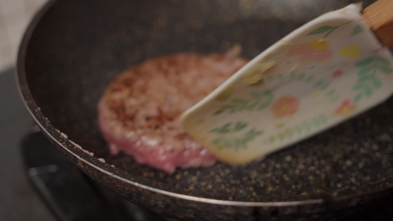 Close-up of a person using a metal spatula to flip a piece of meat on a grill, cooking food making burgers on a ceramic pan