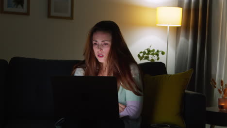 anxious woman sitting on sofa at home at night looking at laptop concerned about social media or bad news 6