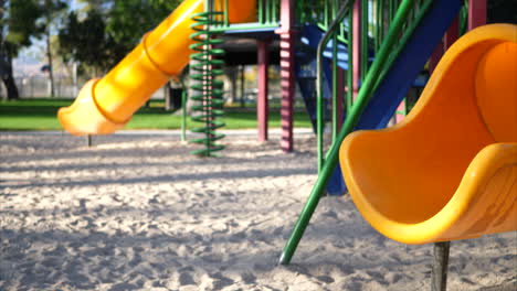 Slide-right-across-a-yellow-slide-in-an-empty-kids-park-playground-with-equipment-and-a-jungle-gym