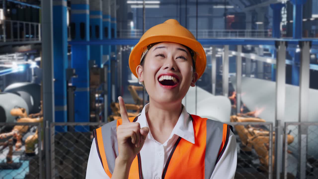 안전 헬을 입은 아시아 여성 엔지니어가 풍력 터빈 제조 공장에서 서서 무언가에 대해 생각하고 주위를 둘러보며 지표손가락을 들어 올립니다.